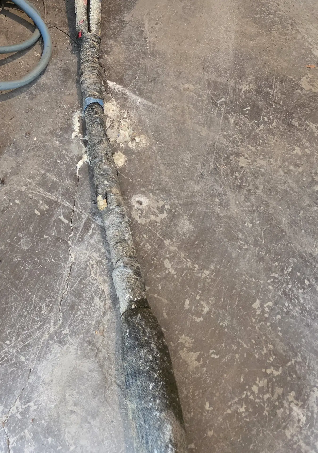 A concrete slab crack with a foam-injection hose and brass fitting alongside -- PolyJacks concrete leveling serving Leawood, KS.